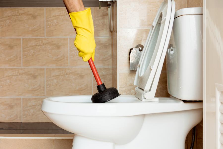 Plumber with a plunger in a clogged toilet